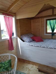 a bed in a wooden cabin with a window at La Roulotte romantique du P'tit Buron in Saint-Saturnin