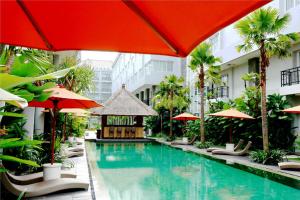 ein Swimmingpool mit Liegestühlen und Sonnenschirmen in einem Hotel in der Unterkunft b Hotel Bali & Spa in Denpasar