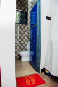 a bathroom with a toilet and a pair of shoes on a red rug at Family Ties in Bagamoyo