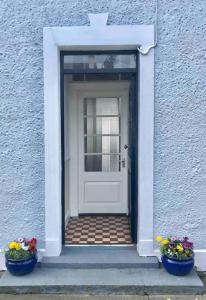 białe drzwi z dwoma kwiatami przed nimi w obiekcie Moville Beach Townhouse on Wild Atlantic Way w mieście Moville