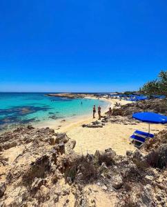 a beach with blue umbrellas and people in the water at Dome Beach Marina Hotel & Resort in Ayia Napa