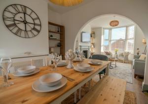 a dining room table with a large clock on the wall at Pebble Cottage - Sea Views, Free Parking & Dog Friendly in Wyke Regis