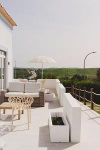 a patio with white furniture and an umbrella at Pure Flor de Esteva in Vila do Bispo