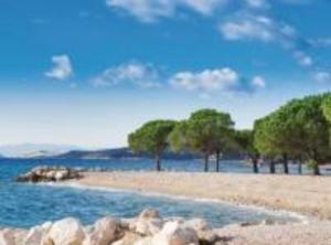 una spiaggia con alcuni alberi, acqua e rocce di Apartments Panorama a Crikvenica