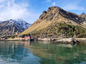 a red house on the water in front of a mountain at Solodden, Authentic rorbu in Lofoten in Sennesvik
