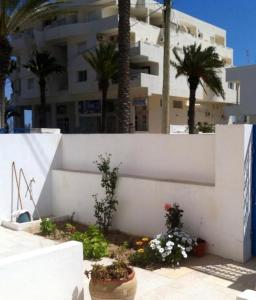 una pared blanca con flores y palmeras frente a un edificio en L'espadon de Mahdia Maison avec petit jardin en Mahdia