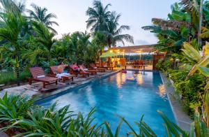 a pool at a resort with chairs and palm trees at New Sunshine Homestay in Hoi An