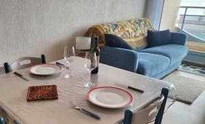 a table with plates and wine glasses and a couch at Appartement face mer in Quend