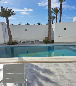 a swimming pool with two chairs and palm trees at villa izabelles in Djerba