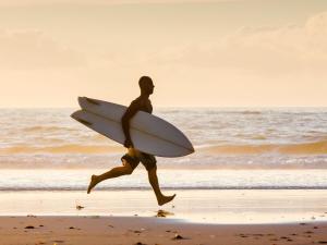 a man running on the beach with a surfboard at SCN City Hotel Rayong in Ban Chang