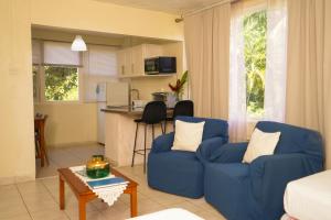 a living room with two blue chairs and a kitchen at Palm Garden Hotel Barbados in Bridgetown