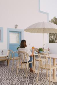 a woman sitting at a table with an umbrella at Pure Fonte Velha B&B in Vila do Bispo