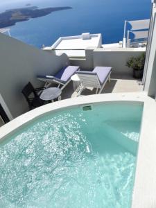 a hot tub on a balcony with chairs and the ocean at Avant Garde Firostefani in Firostefani