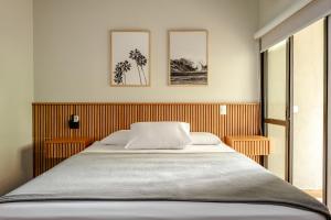 a bed in a bedroom with three pictures on the wall at JQY Beach Flats - 950m da Praia - Garagem subterrânea - Estação de carregamento para veículos elétricos in Juquei