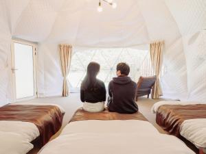 a man and woman sitting in a room looking out the window at Riverside Glamping Kamiseno - Vacation STAY 92770v in Hiroshima