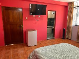 Habitación con pared roja y TV en la pared. en Ñariwalac en Piura