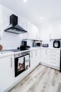 Tranquil 3BR Retreat for Families in Bexleyheath في بيكسليهيث: مطبخ بدولاب بيضاء وفرن علوي موقد