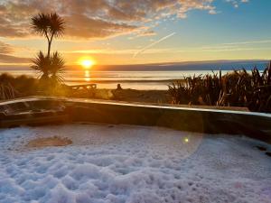 a hot tub with the sunset in the background at Drifting Sands Beachfront Retreat in Hokitika