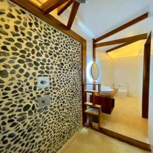 a bathroom with a stone wall with a sink and a mirror at Kawai Duli Bungalows in El Nido