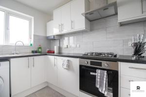 a kitchen with white cabinets and a stove top oven at Newly Launched Two Bedroom House By Den Accommodation Short Lets & Serviced Accommodation With Garden in London