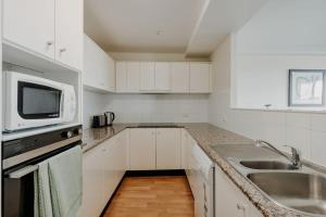 cocina blanca con fregadero y microondas en 2-Bed with Gym, Tennis Court & Stunning Lake Views, en Canberra