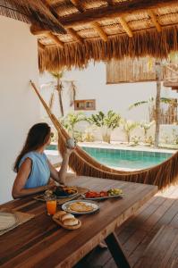 Eine Frau, die an einem Tisch mit Essen und einer Hängematte sitzt. in der Unterkunft Villa Mango Beach Houses in Praia de Moitas
