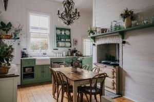 Lake Daylesford Country House في ديلسفورد: مطبخ مع دواليب خضراء وطاولة وكراسي