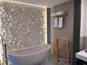 a bath tub in a bathroom with a stone wall at Luminor Hotel Legian Seminyak - Bali in Seminyak