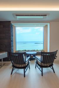 済州市にあるオーシャン グランド ホテルの椅子2脚とテーブル、大きな窓が備わる客室です。