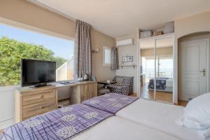 a bedroom with a bed and a tv and a window at Roc Hotel - Hôtel 4 étoiles les pieds dans l'eau in Le Lavandou