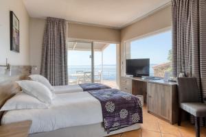 um quarto com uma cama, uma televisão e uma janela em Roc Hotel - Hôtel 4 étoiles les pieds dans l'eau em Le Lavandou