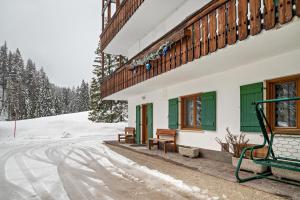 a building with green doors and benches in the snow at Appartamento Aurone in Arabba