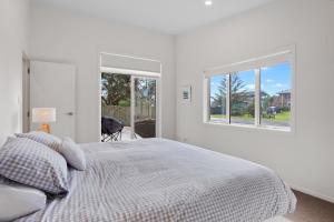 een witte slaapkamer met een bed en 2 ramen bij Modern Kiwi Bach - Waihi Beach Holiday Home in Waihi Beach