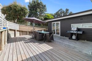 een houten terras met een tafel en een grill bij Modern Kiwi Bach - Waihi Beach Holiday Home in Waihi Beach