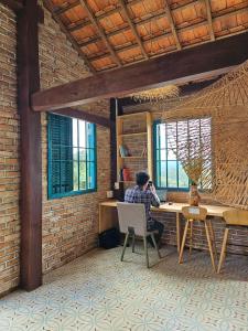 un homme assis à un bureau dans une pièce en briques dans l'établissement Nhà Gạch cổ - Antique Brick House, à Bảo Lâm