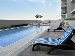 una piscina con 2 tumbonas junto a un edificio en Aura Azizi by Golden Casa, en Dubái