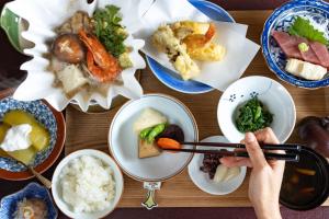 a person holding a pair of chopsticks over a table of food at Temple Hotel 岸之坊 in Minobu