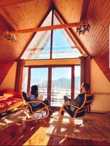 dwoje osób siedzących w fotelach w pokoju z dużym oknem w obiekcie Ethno village Montenegro Brezna w mieście Plužine