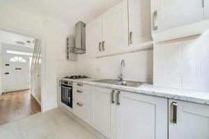 una cucina bianca con armadi bianchi e lavandino di A Luxurious 3 Bed-Terrance House a Londra