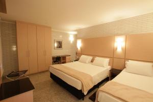 a hotel room with two beds and a desk at Hotel Confiance Centro Cívico in Curitiba