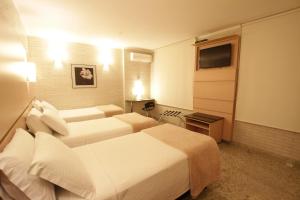 a hotel room with two beds and a television at Hotel Confiance Centro Cívico in Curitiba