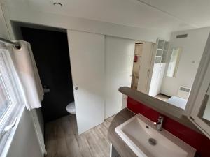 La salle de bains blanche est pourvue d'un lavabo et d'un miroir. dans l'établissement MobilHome Comfort XL (37m2) : 2 Chambres (6 personnes) - 2 SDB - Clim centralisée - TV - Terrasse balcon, à Cadenet