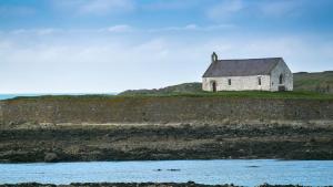 an old house on a hill next to a body of water at Penrhyn Isaf Dau in Aberffraw