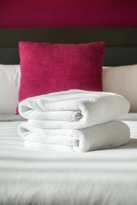 una pila de toallas blancas en una cama con una almohada rosa en Marigold Celebration hotel, en Rāipur