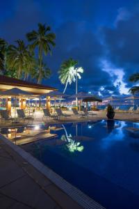 a swimming pool with chairs and palm trees at night at Jatiuca Hotel & Resort in Maceió