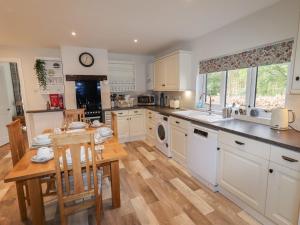 cocina con armarios blancos, mesa y fregadero en Beau Cottage en Bewdley