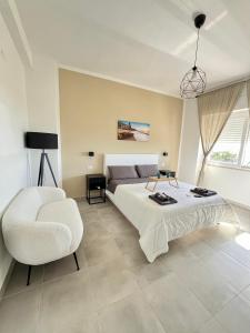 a white bedroom with a bed and a chair at Esclusivo alloggio a sfioro sul mare con terrazza. in Santa Maria di Castellabate