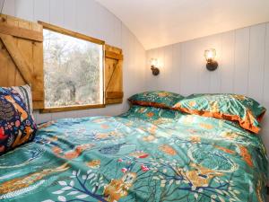 a bedroom with a bed with a colorful comforter and a window at The Foxes Den Shepherds Hut in Bristol
