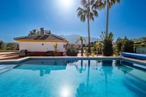 a swimming pool in front of a house with palm trees at Casa Amarilla Casitas in Alhaurín el Grande