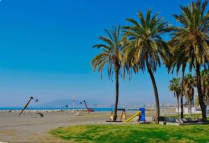 um parque com baloiços e palmeiras na praia em Apartamento El Dorado cerca del mar em Málaga